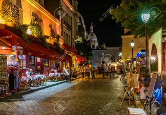 Typical night view of cozy street with tables of cafe and easels of street painters in quarter Montmartre in Paris, France